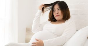 Pregnant woman in white looking at her hair.